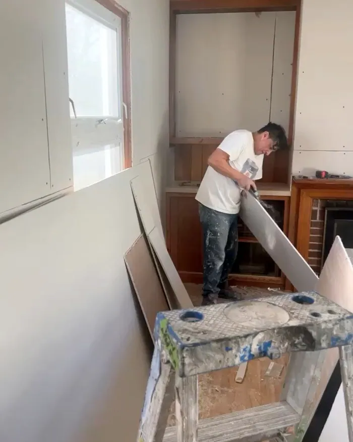 A painter hanging sheetrock over old paneling